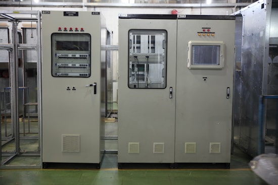 Industrial control panels with various buttons, switches, and display screens are placed in a well-lit environment. The setup suggests a technical or engineering setting with panels housing electronic or communication equipment.