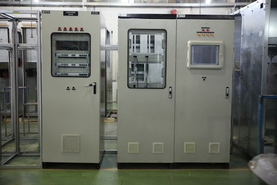 Industrial control panels with various buttons, switches, and display screens are placed in a well-lit environment. The setup suggests a technical or engineering setting with panels housing electronic or communication equipment.