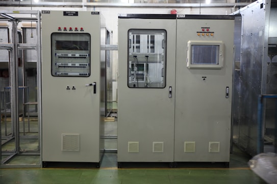 Industrial control panels with various buttons, switches, and display screens are placed in a well-lit environment. The setup suggests a technical or engineering setting with panels housing electronic or communication equipment.