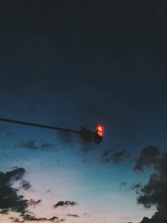 A traffic light showing red with a 43-second countdown is suspended against a backdrop of a darkening sky. Clouds are scattered, and the mix of dark blues and subtle oranges suggests an evening setting.