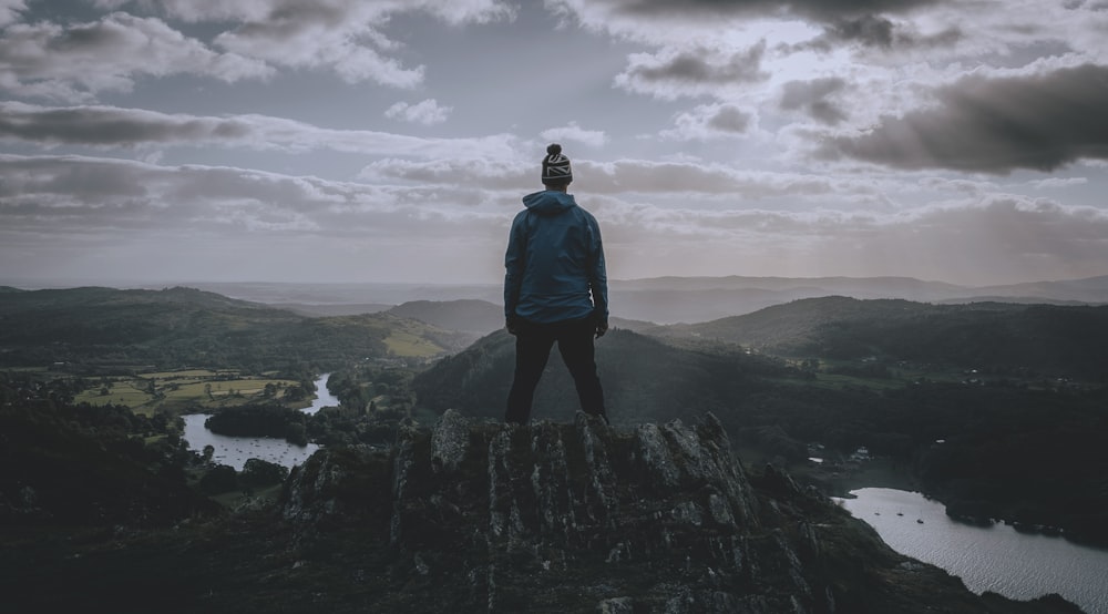 man in black jacket standing on rock formation under cloudy sky during daytime