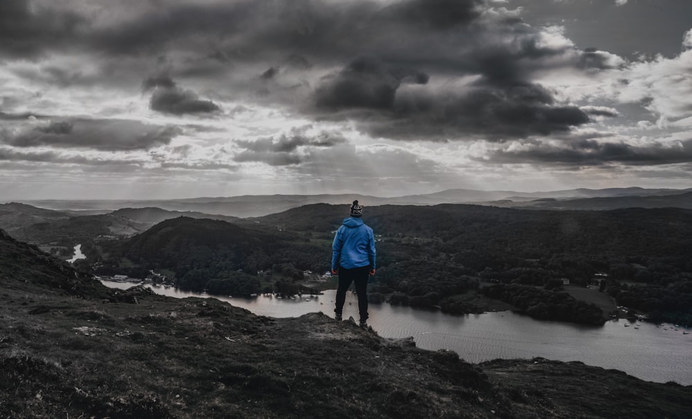 man in blue jacket standing on brown rock formation under gray clouds during daytime