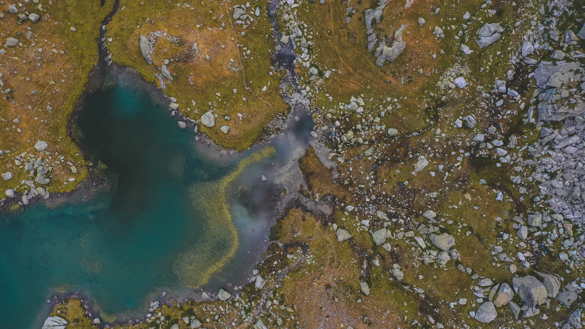 A drone view of a small mountain lake among grass and boulders near Vielha