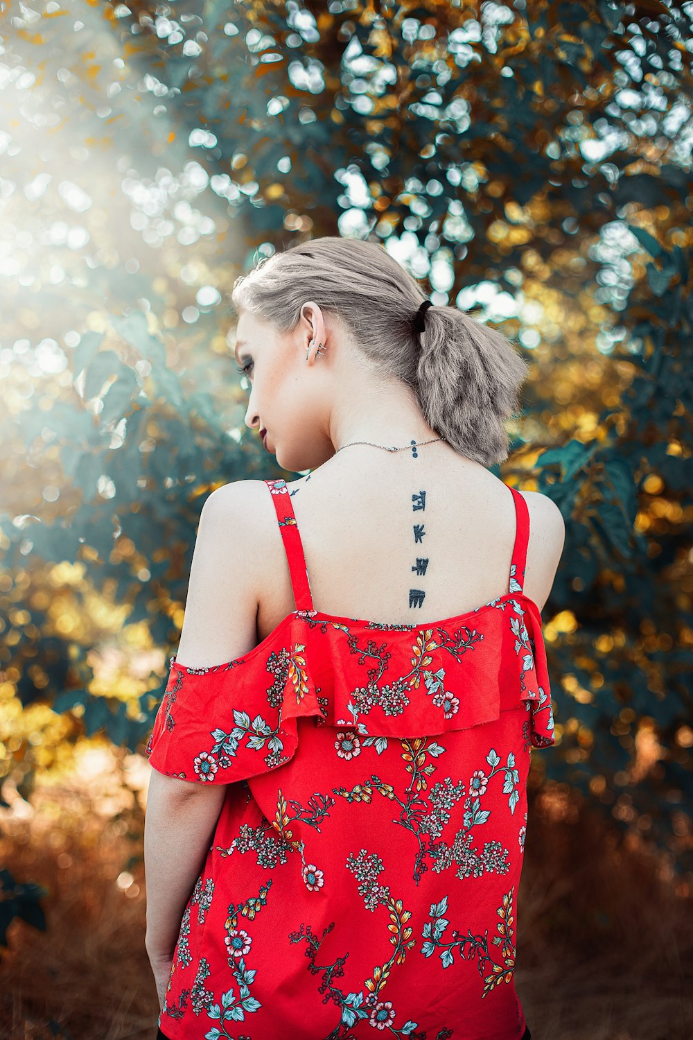 woman in red and white floral sleeveless dress standing near green trees during daytime