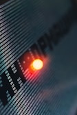 Binary code runs across a digital screen, highlighted by a glowing red-orange LED light. The numbers are aligned in a matrix pattern, creating a sense of digital complexity and data flow.