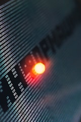 Binary code runs across a digital screen, highlighted by a glowing red-orange LED light. The numbers are aligned in a matrix pattern, creating a sense of digital complexity and data flow.