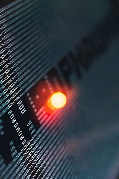 Binary code runs across a digital screen, highlighted by a glowing red-orange LED light. The numbers are aligned in a matrix pattern, creating a sense of digital complexity and data flow.