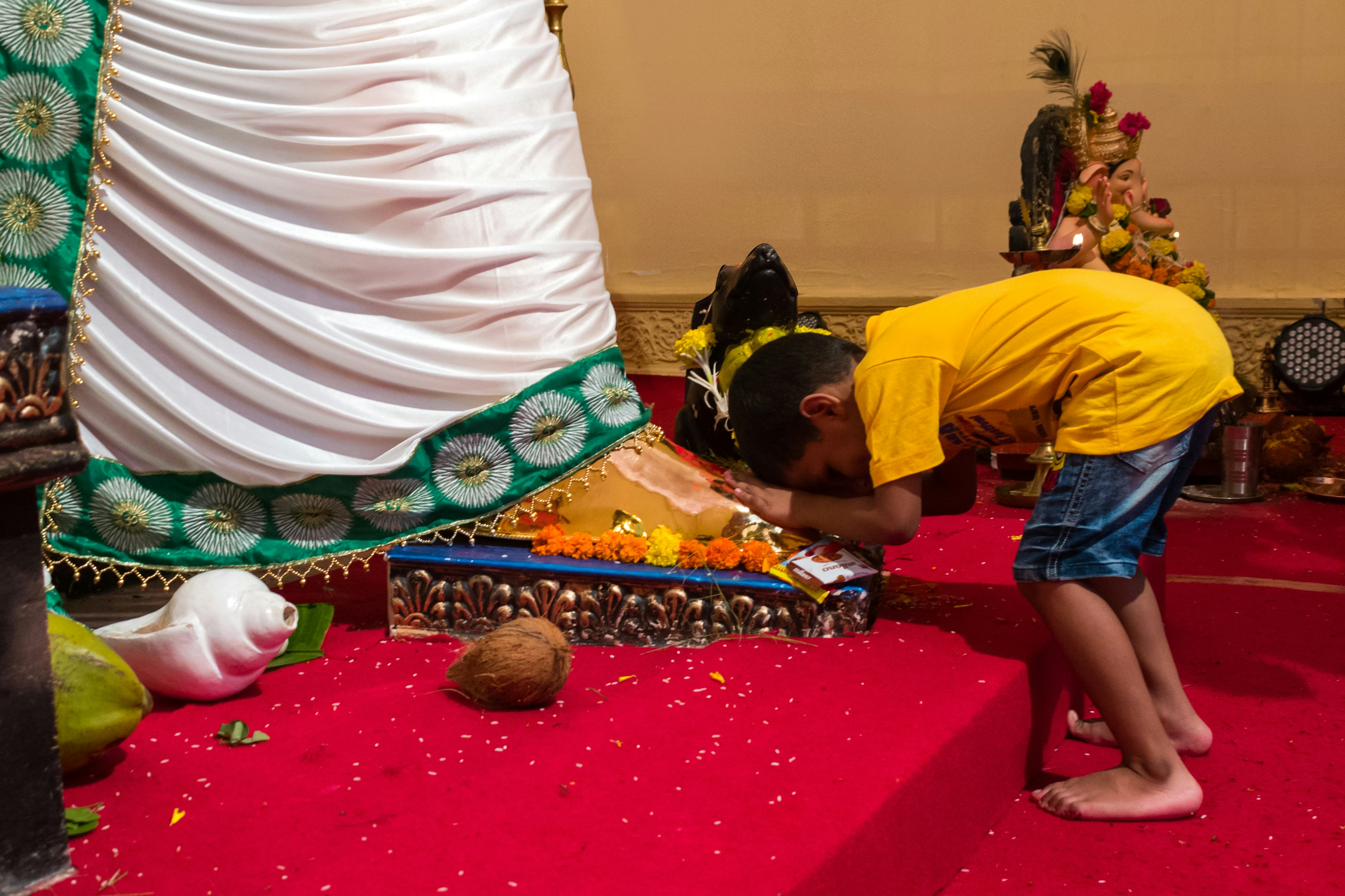 man in yellow t-shirt sitting on red carpet, A boy seeking Lord Ganesha