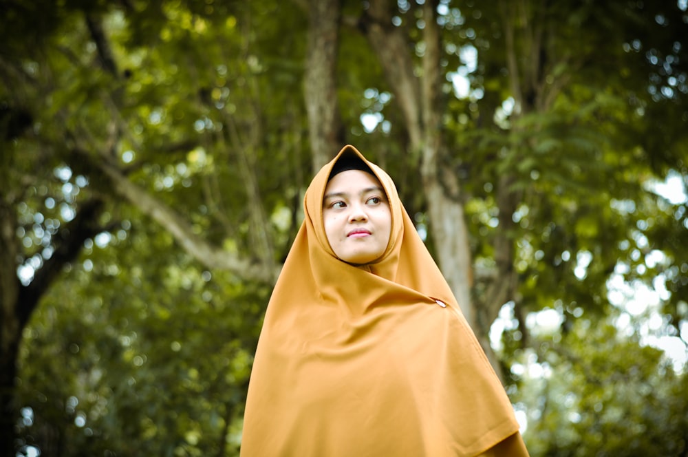 woman in yellow hijab standing near green trees during daytime