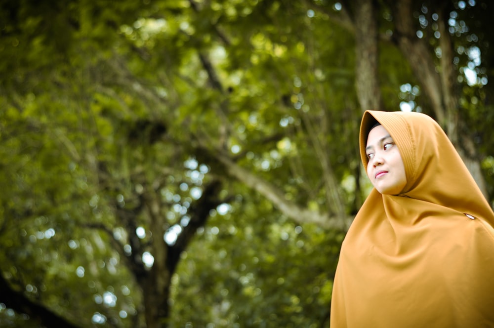 woman in brown hijab standing near green trees during daytime