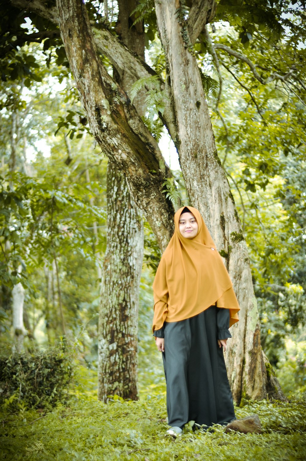 woman in yellow hijab standing beside brown tree