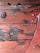 Weathered wooden surface with peeling red paint, revealing aged wood beneath. Large round metal bolts secure the planks.