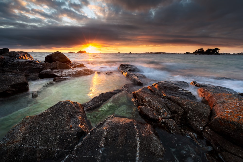 rocky shore under cloudy sky during sunset