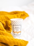 A polka-dot mug with the text 'Make Today So Awesome' is positioned on a soft, yellow knitted fabric that appears to be a blanket. The scene suggests a cozy and positive atmosphere.