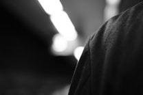 An abstract black and white photograph showing a close-up of a fabric texture on the right side, with blurred lights and shadows in the background.