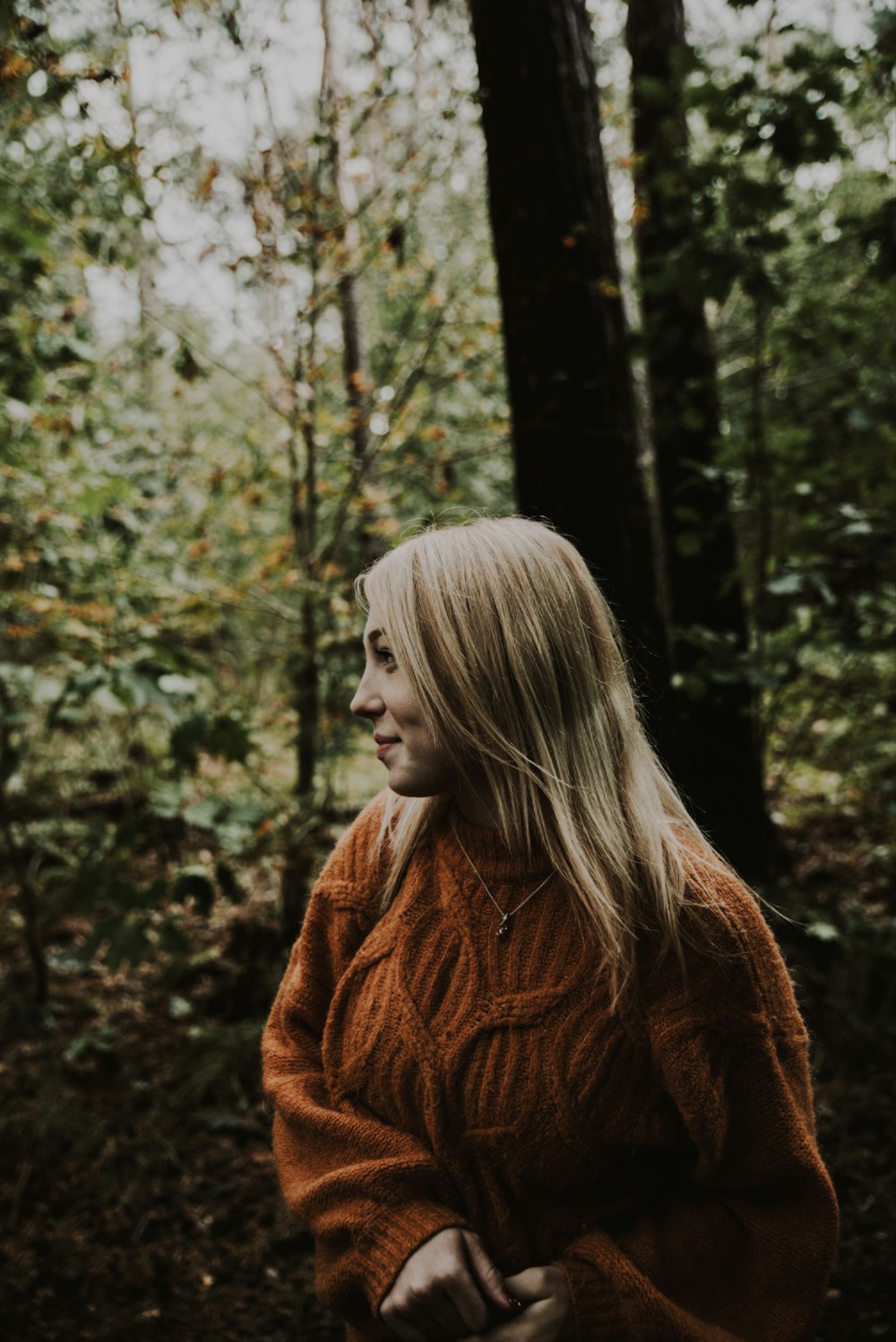 Donna in maglione di maglia marrone in piedi vicino agli alberi verdi durante il giorno