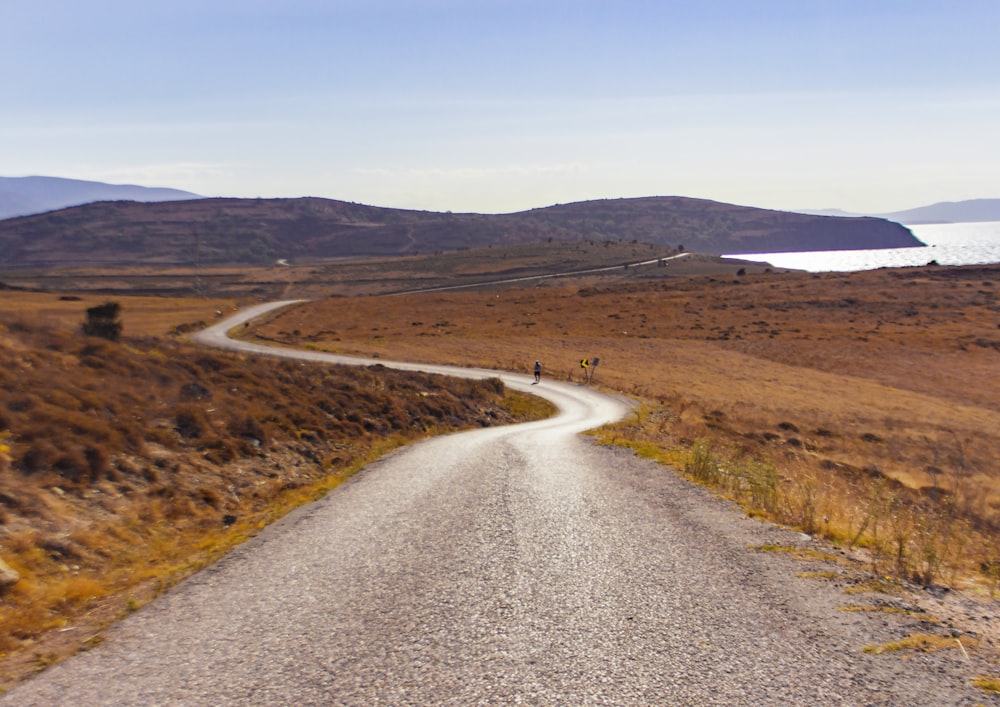 gray asphalt road between brown grass field during daytime