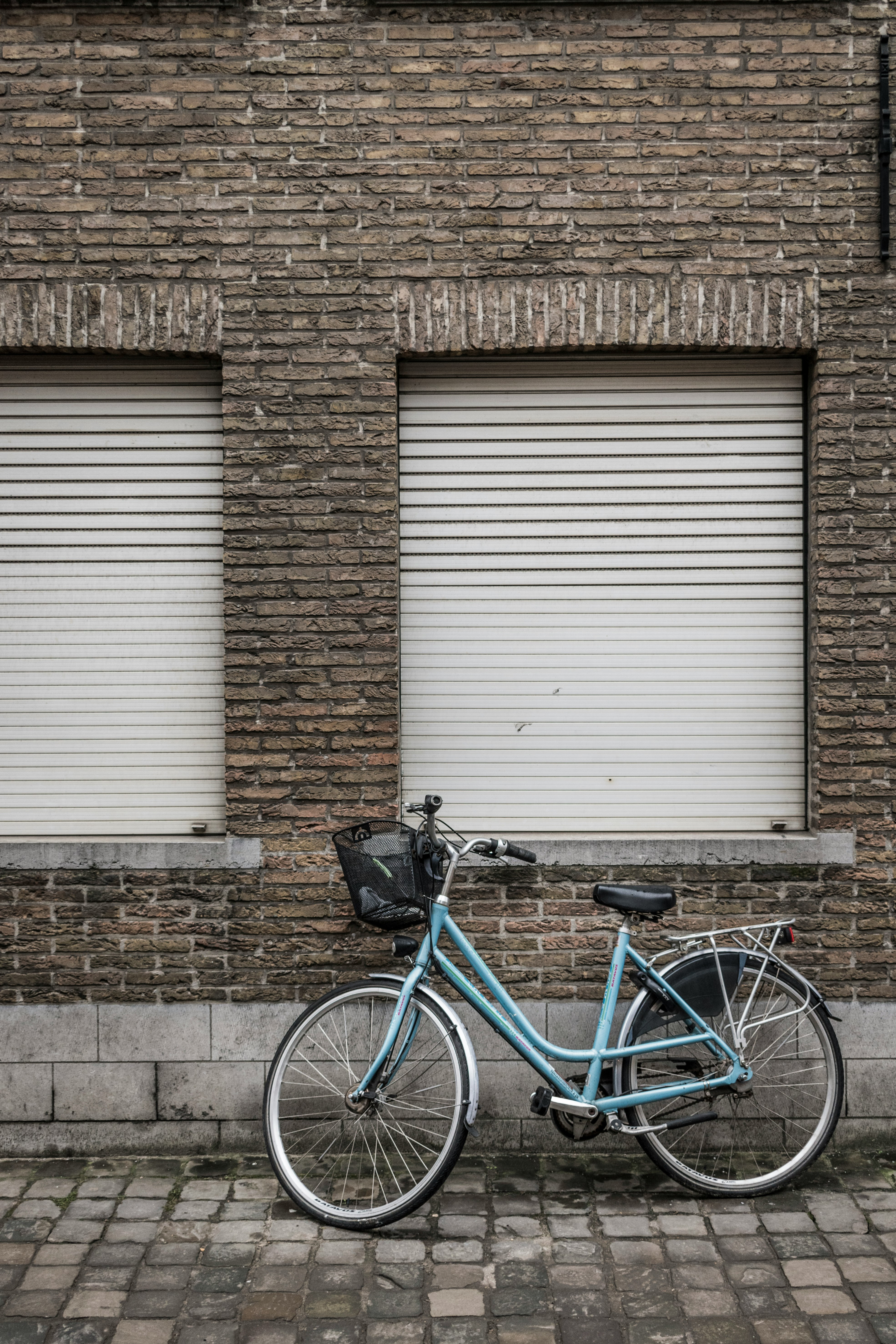 blue city bike parked beside brown brick wall