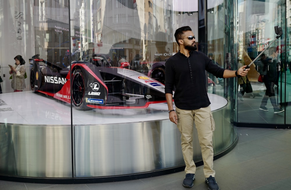 man in black crew neck t-shirt and brown pants standing beside red and white ferrari