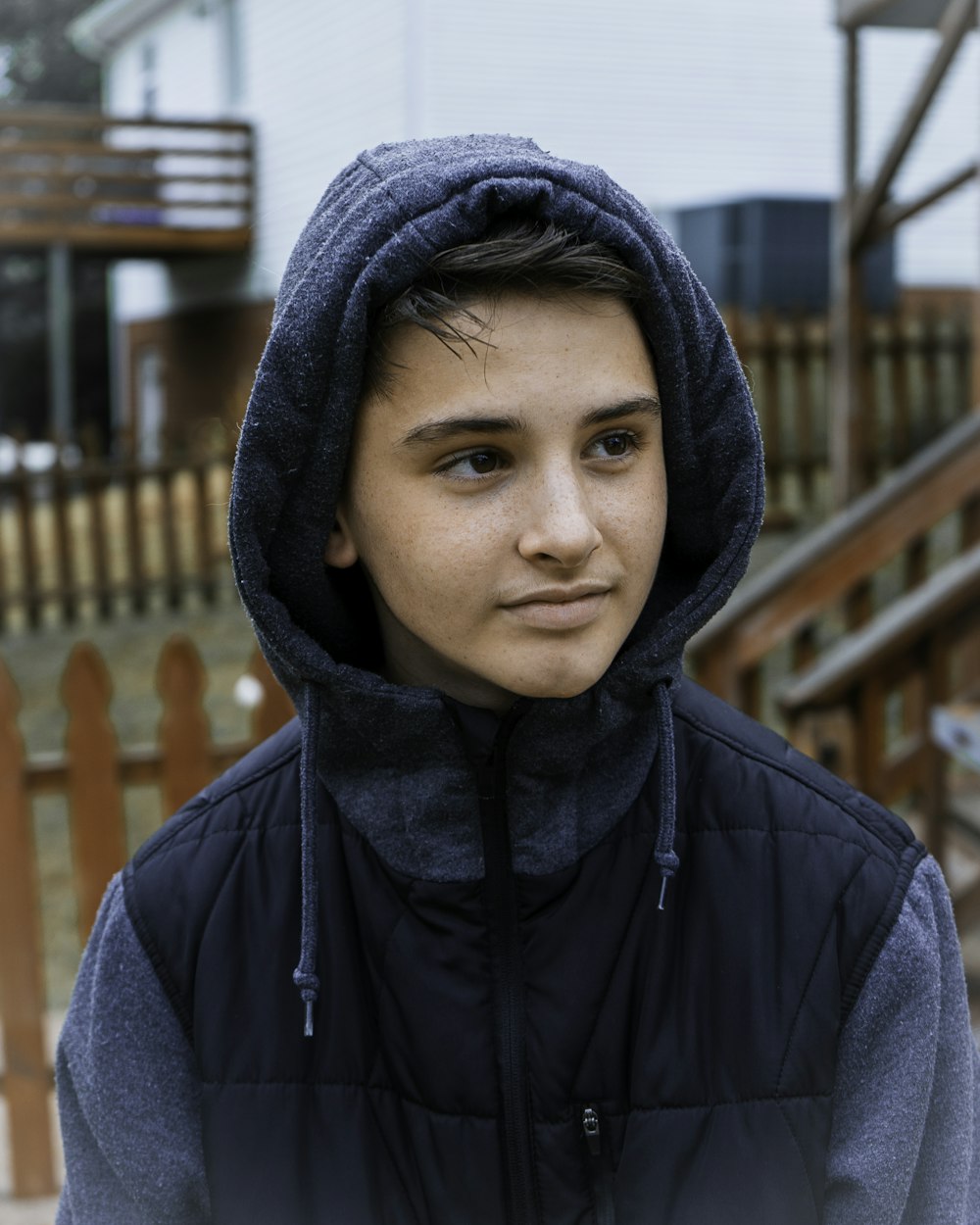 man in black hoodie standing near brown wooden fence during daytime