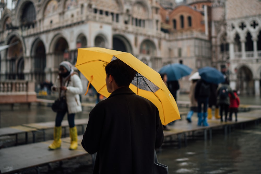 hombre con abrigo negro sosteniendo paraguas amarillo