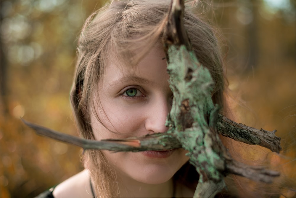 girl in white tank top holding green tree branch