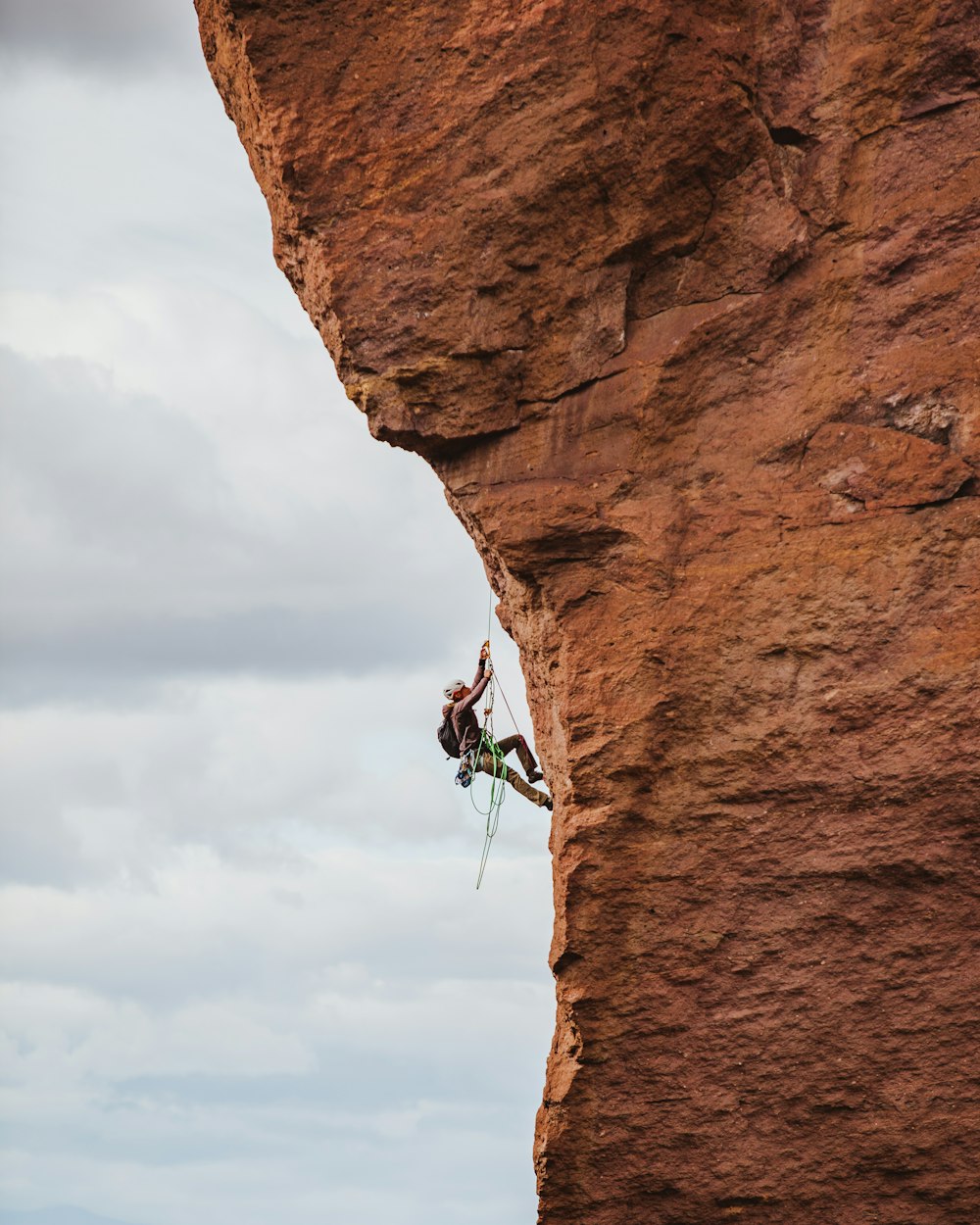 homem de calções pretos escalando a formação rochosa marrom durante o dia