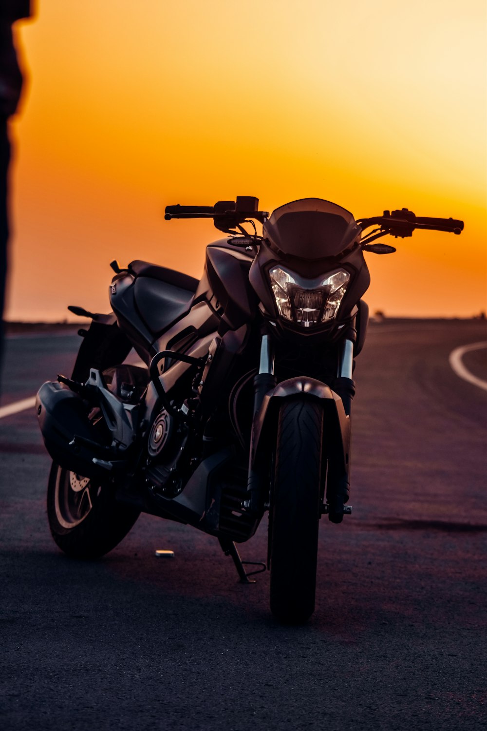 Schwarzes Motorrad auf grauer Asphaltstraße bei Sonnenuntergang