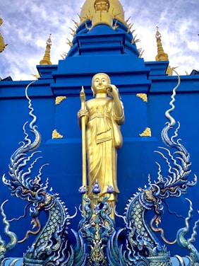 A majestic statue of Sun Go Kong holding a massive golden staff against a dramatic sky.