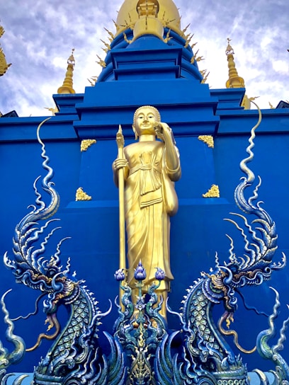 A majestic statue of Sun Go Kong holding a massive golden staff against a dramatic sky.