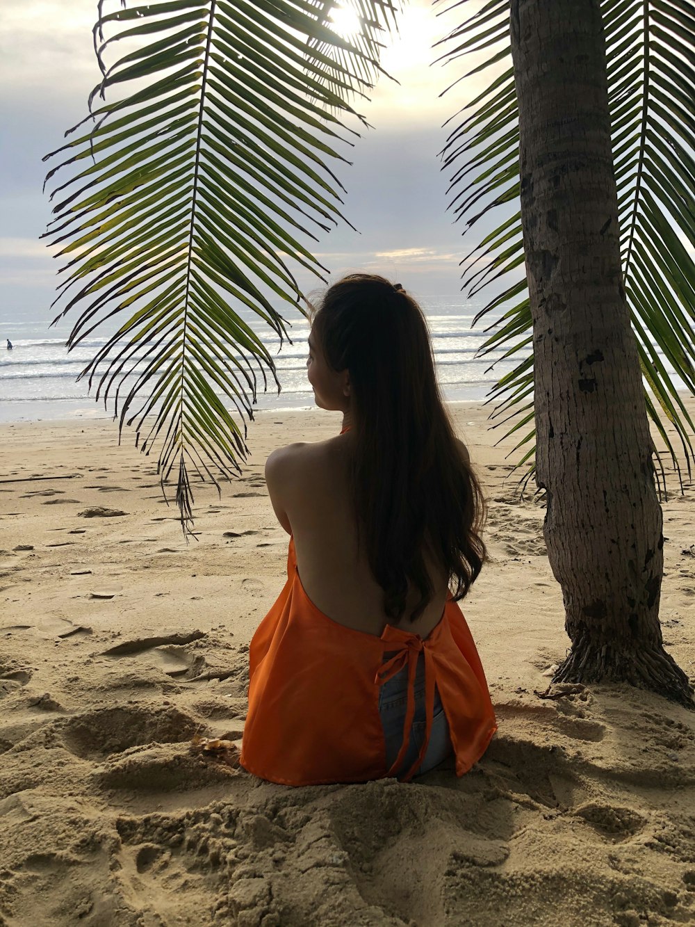 Frau in orangefarbenem Kleid sitzt tagsüber am Strand