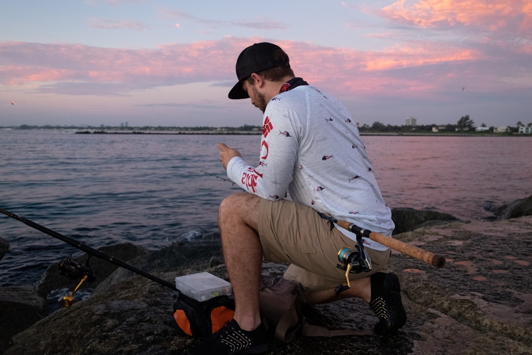 man in white long sleeve shirt sitting on black and brown fishing rod near body of on on on on