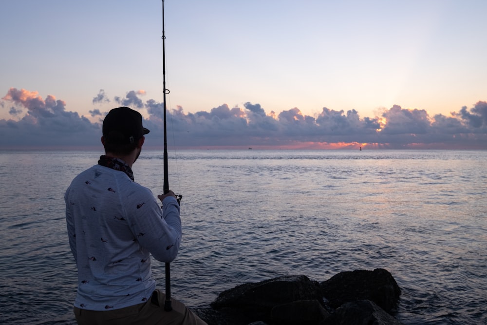 man in white dress shirt fishing on sea during sunset