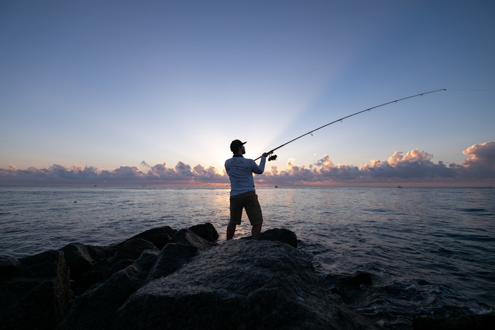 Mann in weißem T-Shirt und braunen Shorts beim Fischen auf See tagsüber