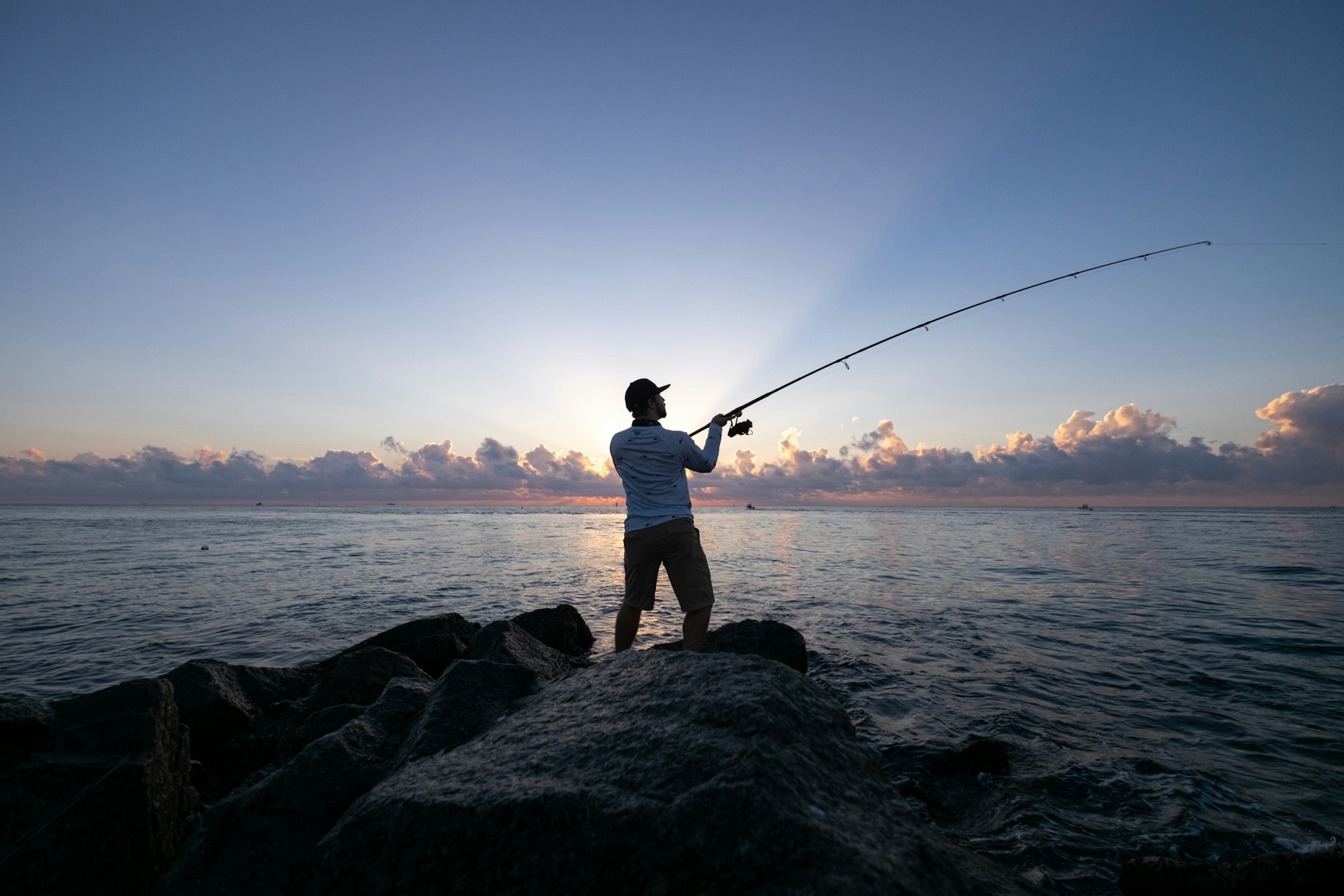 Man fishing on jetty at dawn.
