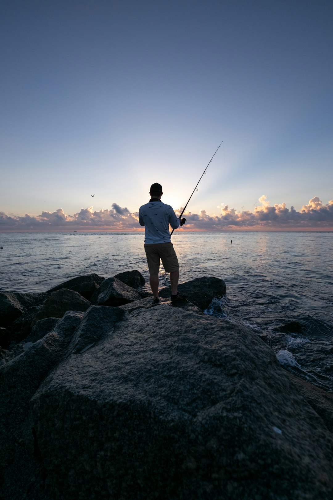 man in white shirt and brown shorts fishing on sea during daytime