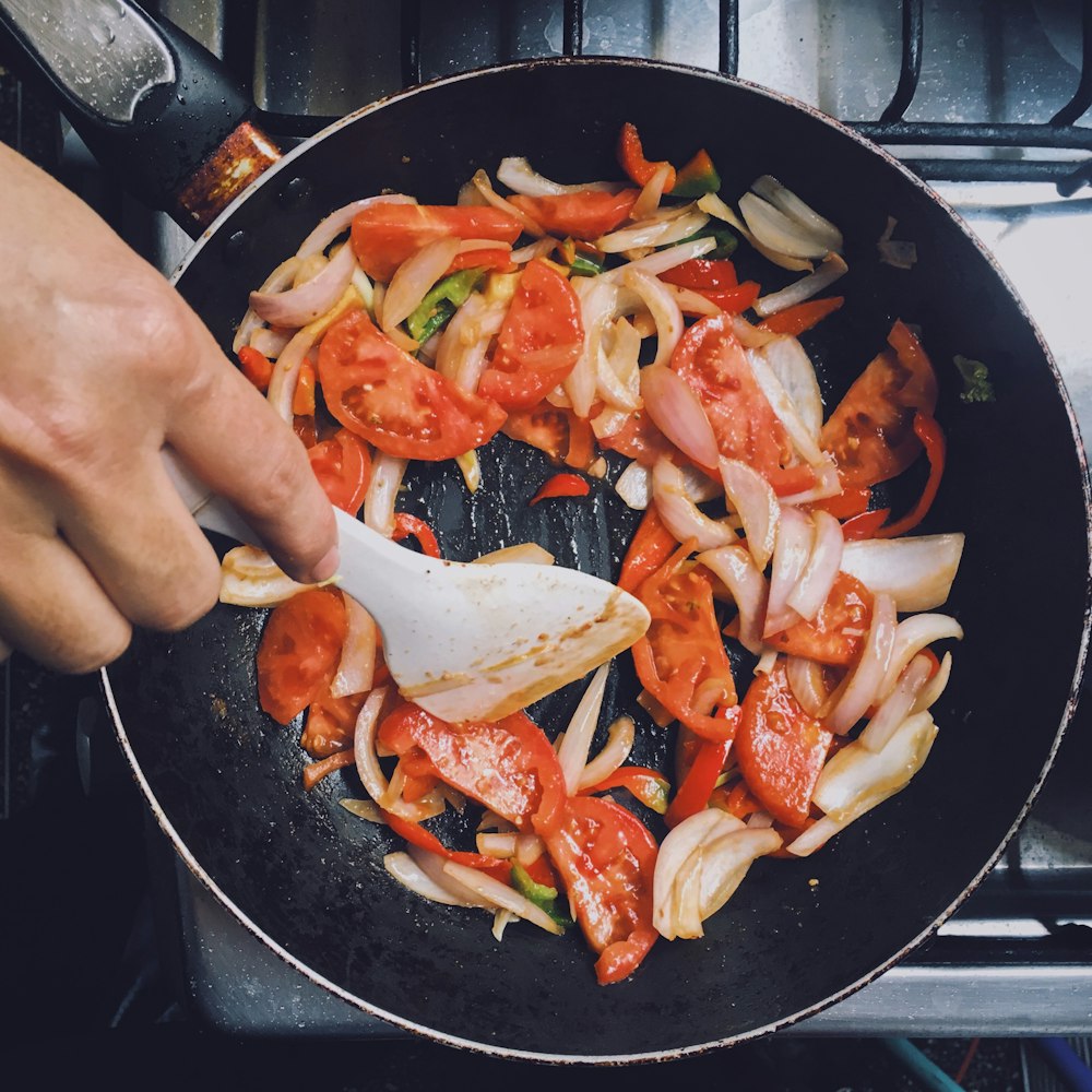 person holding black frying pan with cooked food