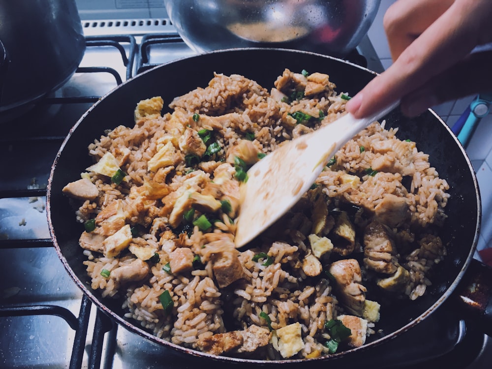 person holding black frying pan with fried rice
