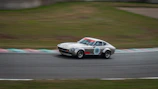 A dynamic shot of a classic racing car speeding on a track, tires kicking up dust.