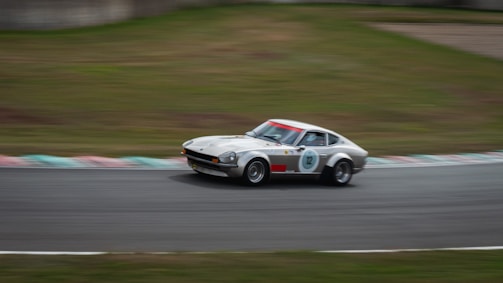 A vintage car is captured in motion on a race track, showcasing its aerodynamic design and classic features. The background is blurred, emphasizing the speed of the vehicle as it navigates a curve on the track.