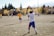 A group of young soccer players is on a grassy field. One player in a white jersey with '11' printed on the back is preparing to throw the ball. Other players are wearing yellow jerseys. The backdrop consists of trees with autumn foliage and a residential area.