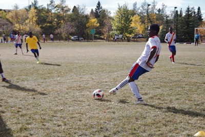 boy in white shirt and red shorts playing soccer during daytime congo zoom background