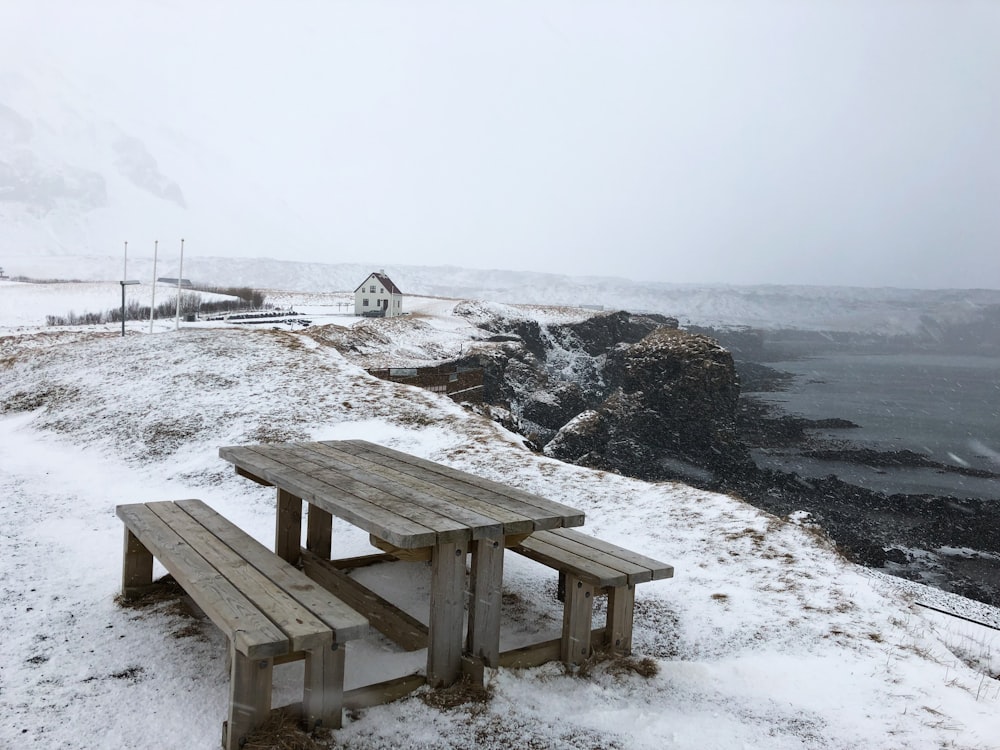 brown wooden picnic table on snow covered ground near body of water during daytime