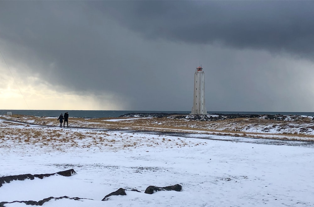 people walking on snow covered field near white lighthouse under gray cloudy sky during daytime