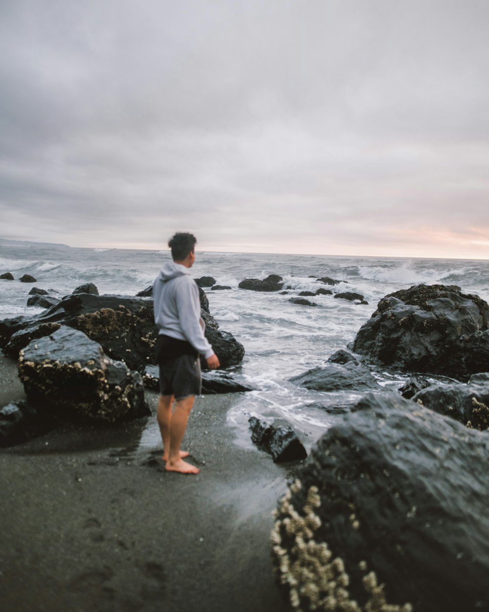 man in white long sleeve shirt and black pants standing on rocky shore during daytime