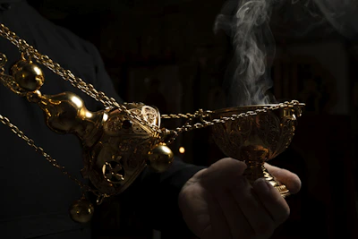 Hands holding a handcrafted wooden defumador stick against a soft red and black background.