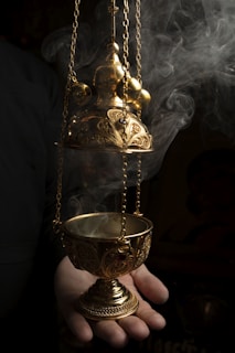 person holding gold colored vase with white smoke