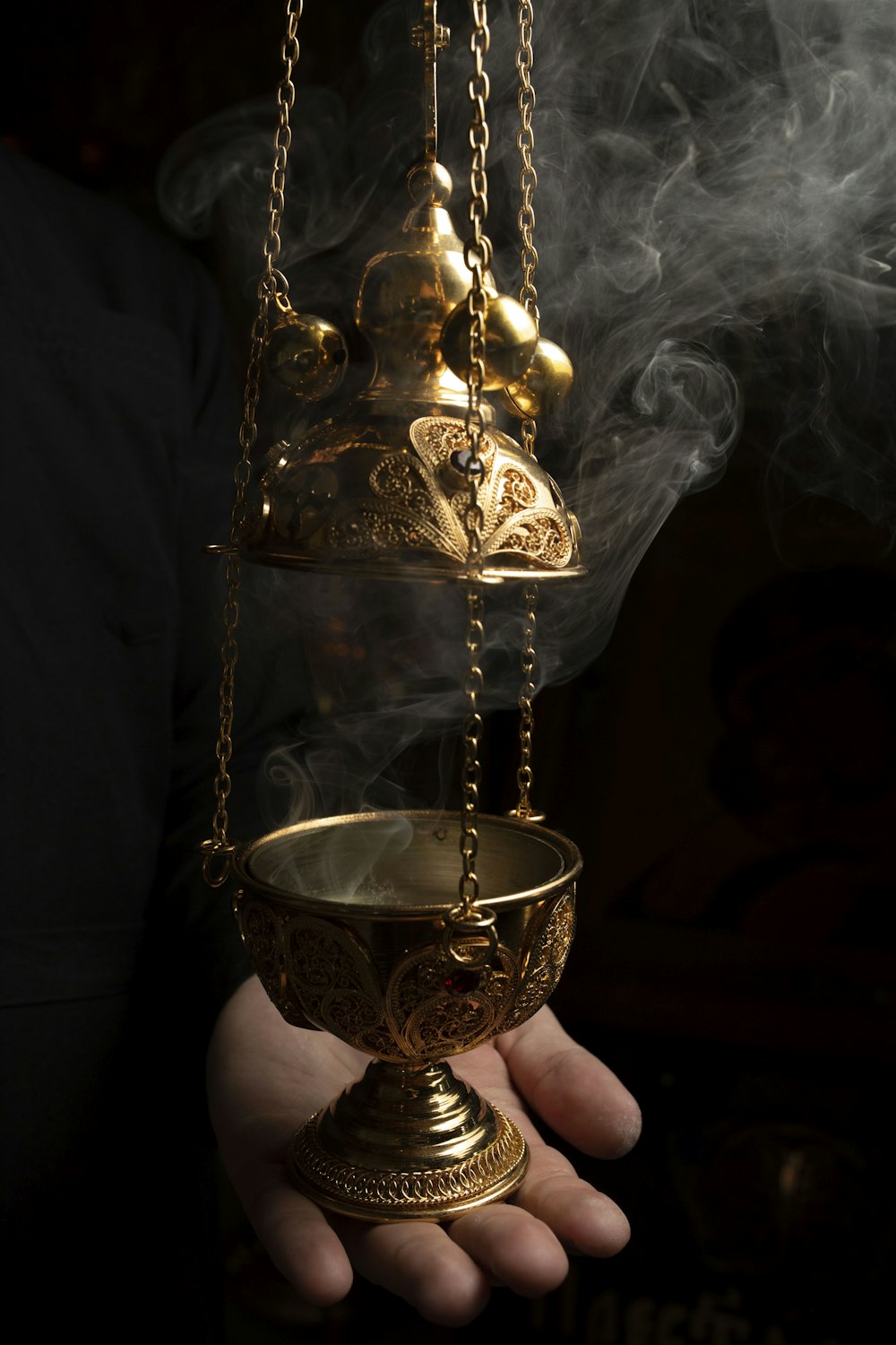 person holding gold colored vase with white smoke