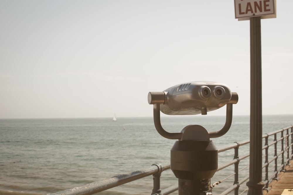 gray and black binoculars on gray metal railings near sea during daytime