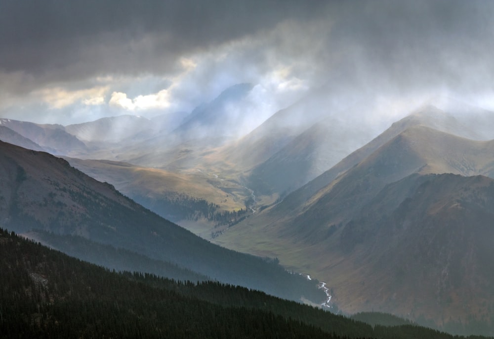 green trees near mountain under white clouds during daytime